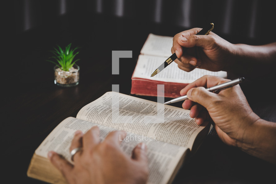 Two people studying the Bible with pens