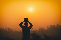 silhouette of a boy holding up a Bible at sunset 