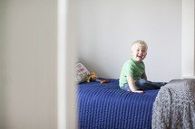 happy toddler boy sitting on a bed.