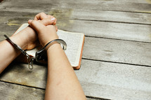 handcuffed praying hands on the pages of a Bible 