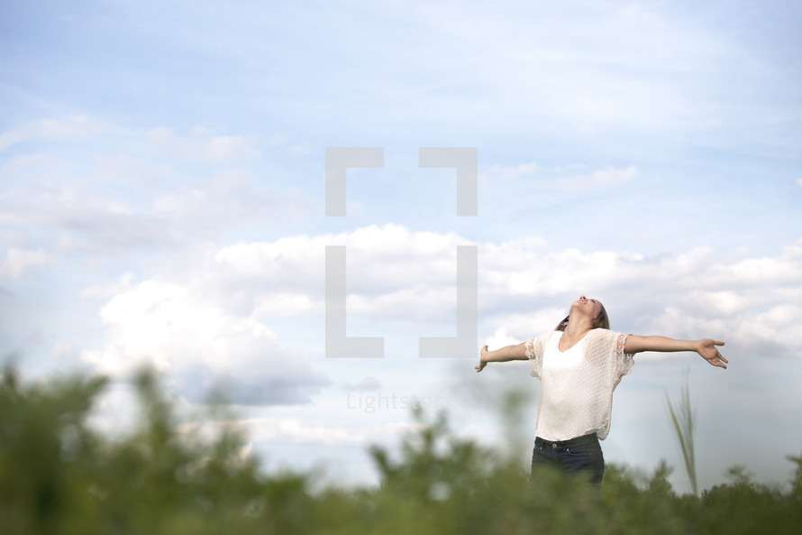 Woman standing outdoors with arms extended looking up the heavens.