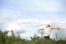Woman standing outdoors with arms extended looking up the heavens.