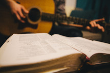 A man playing a guitar and an open Bible. 