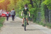 boy riding a bike on a path wearing a face mask 
