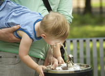 A man holding a young child up to a water fountain.