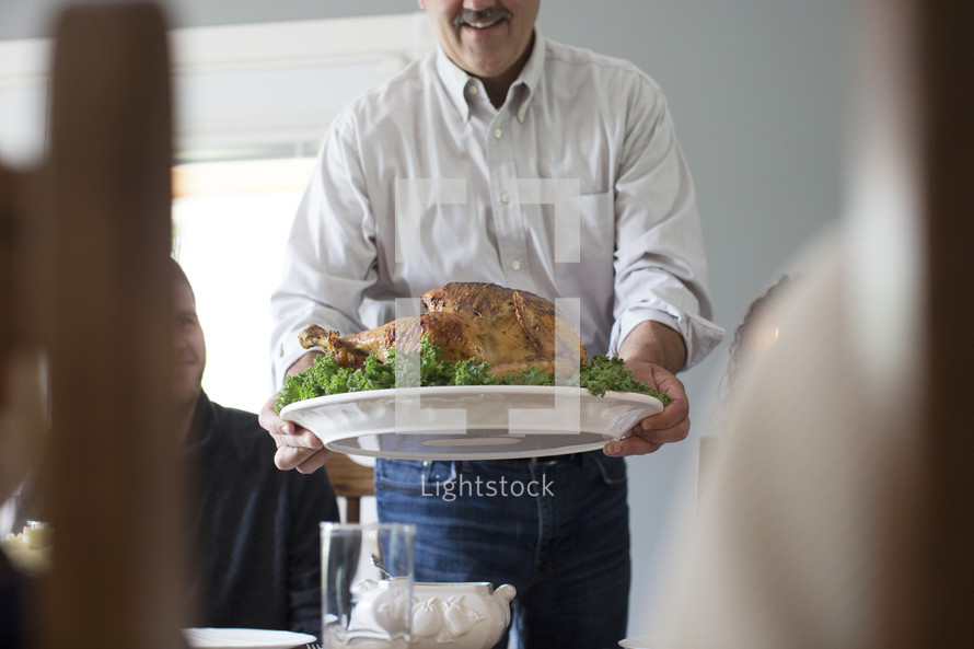 a man presenting the turkey to the table at Thanksgiving 