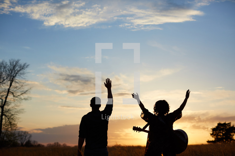 man and a woman standing in a field with a guitar at sunset 