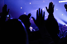 silhouettes of raised hands at a concert 