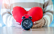 person holding a red heart and alarm clock, valentine day background.