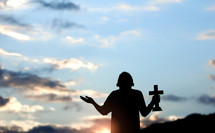 Silhouette of young male christian standing and holding a cross 