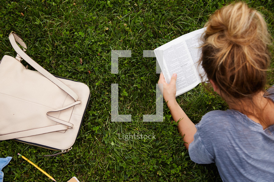 a woman lying in the grass reading a Bible.