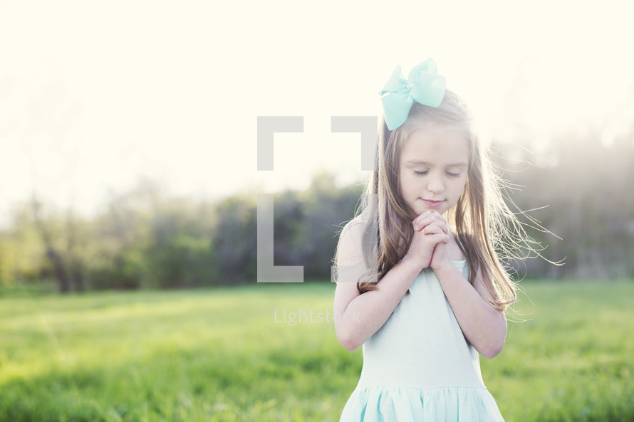 a girl with praying hands in a field of green grass