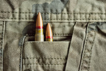 Two rifle bullets hidden into military camo pocket pants. Military ammunition