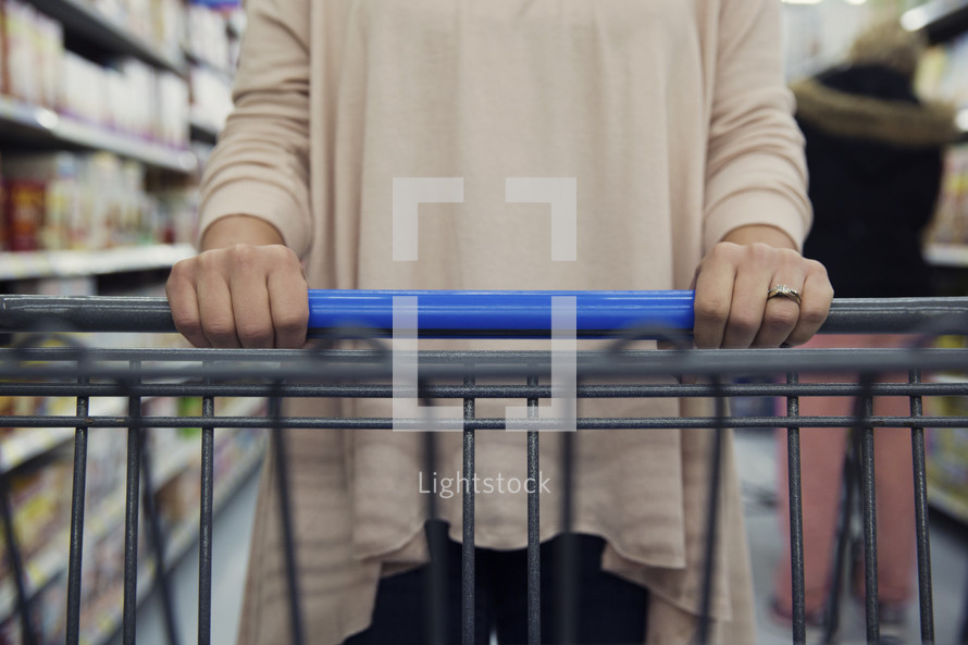 a woman pushing a shopping cart in a grocery store. 