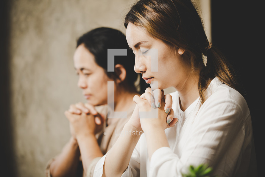 Two Asian women praying to God together in church.