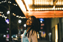 Smiling woman standing outside under a marquee of lights.