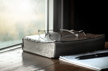 A Bible and reading glasses in a window 