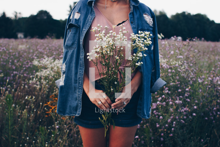 a woman walking through a field picking flowers 