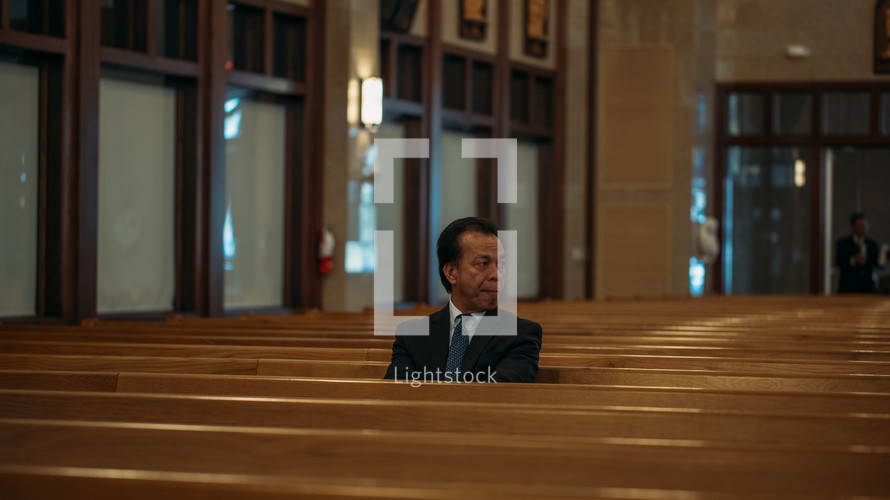 man in a suit sitting alone in a church 