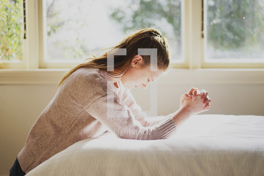 a woman kneeling in prayer by her bed