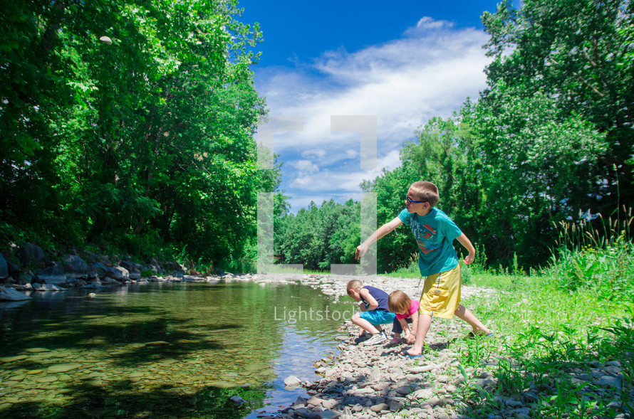 children tossing rocks across a stream 