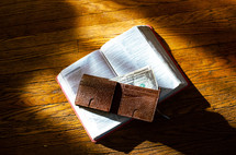 wallet with cash on the page of a Bible 