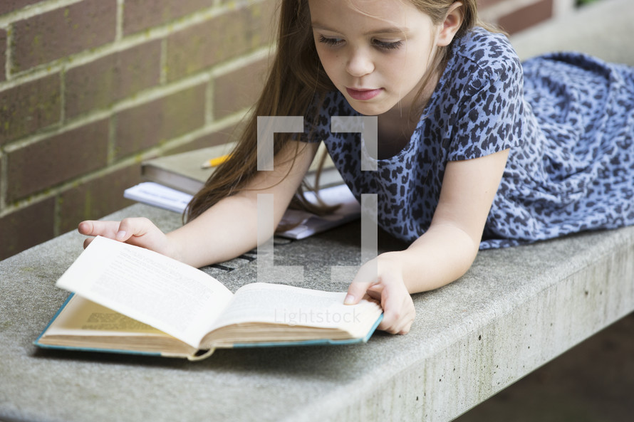 a child on a bench reading a book while waiting for school to start 