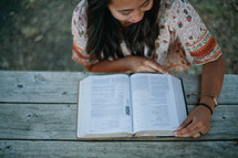 woman reading a Bible outdoors at a picnic table 