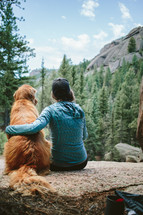 a woman sitting on a rock with her golden retriever dog 