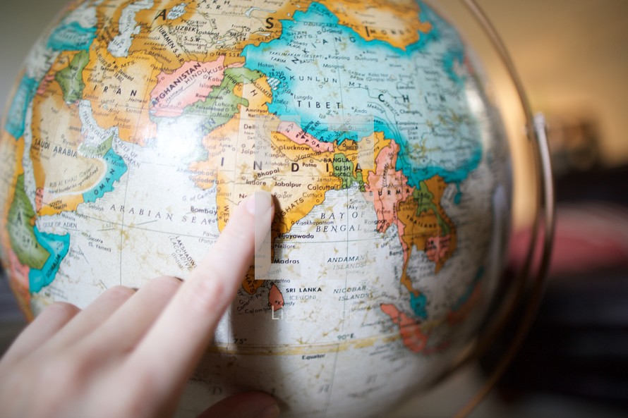 a finger pointing to India on a globe 