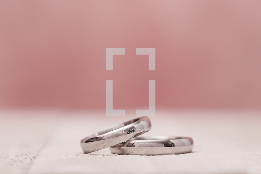 Macro View of Wedding Rings on a Wooden Table with Pink Background