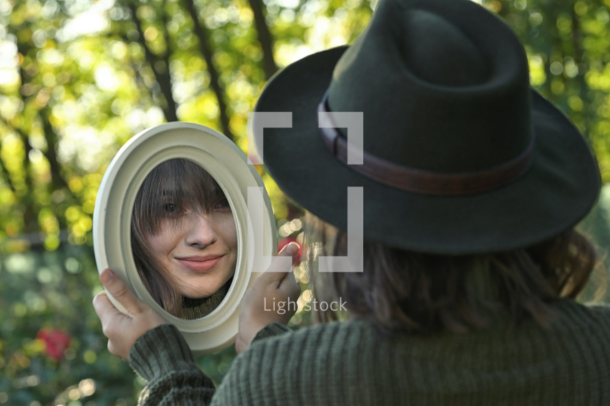 a young woman looking in a mirror outdoors 