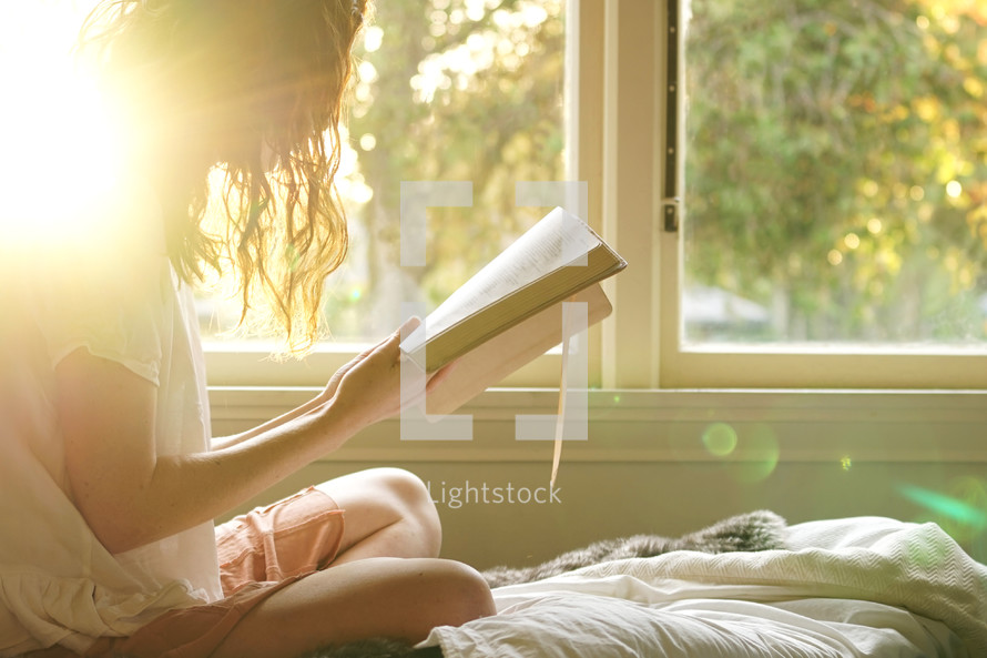teen girl sitting on a bed reading a Bible 