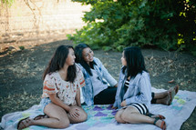 friends sitting on a blanket in the grass talking 