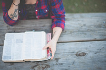 Woman reading the BIble at an outdoor picnic table.