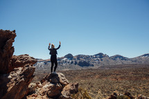 Woman standing on a rock in the dessert with raised hands 