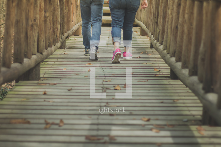 Two women walking down a wooden bridge