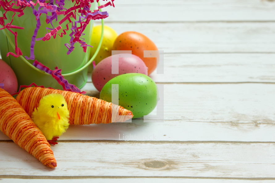 Easter eggs and carrot decorations in an Easter basket on white wood boards 