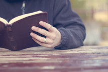 man reading a Bible at a picnic table 