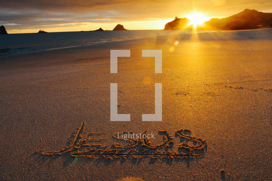 Jesus written in the sands of a beach at sunset 