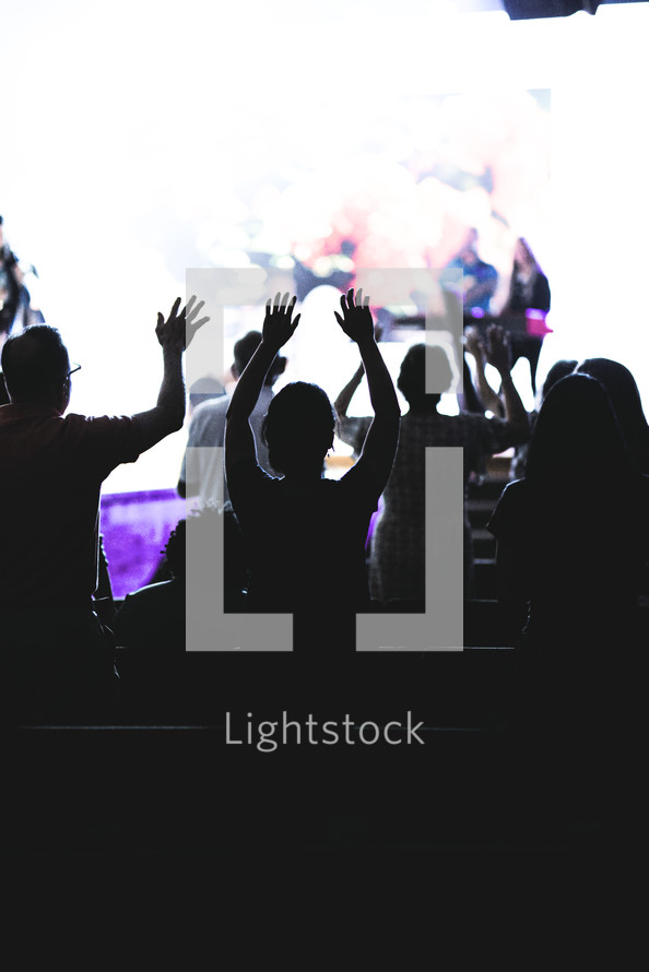 silhouettes of people with hands raised at a worship service 
