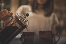 A woman pouring coffee into a mug from a french press