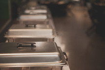Stainless steel pans lined up for catering a meal.