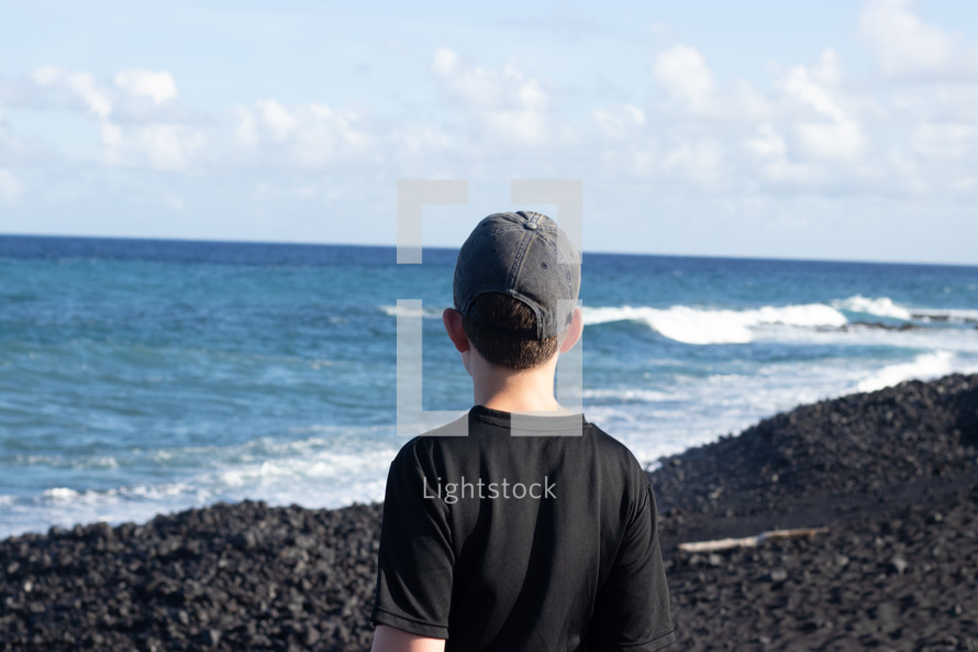 boy standing on a volcanic beach 