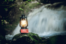 lantern on a mossy rock in front of a waterfall 
