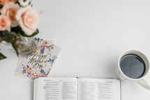 an open Bible, mother's day card, coffee cup, and bouquet of flowers 
