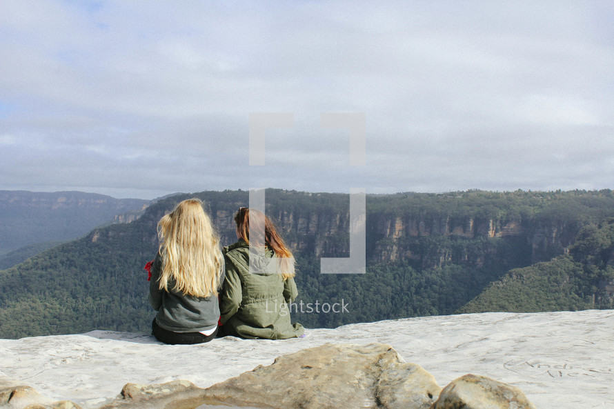 two women sitting at the top of a mountain 