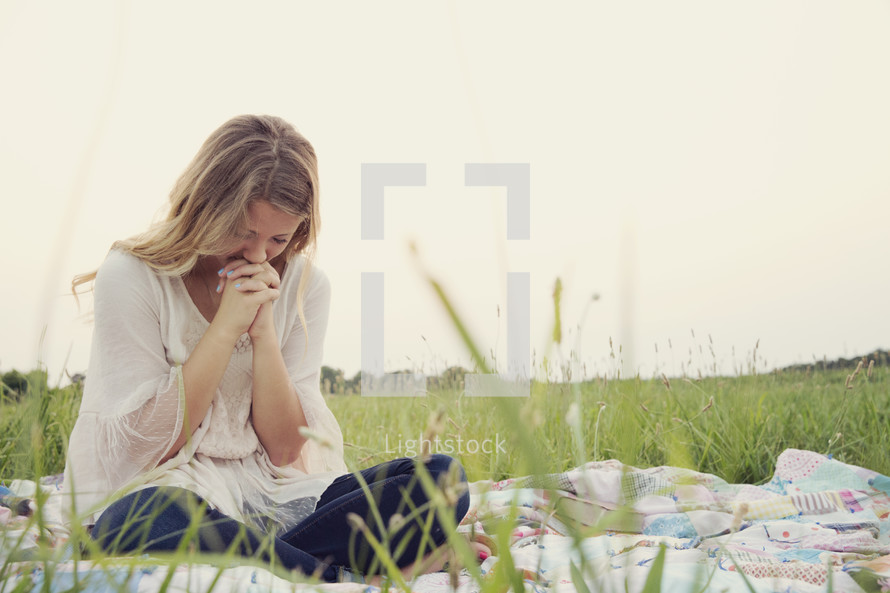 woman sitting on a blanket in the grass praying 