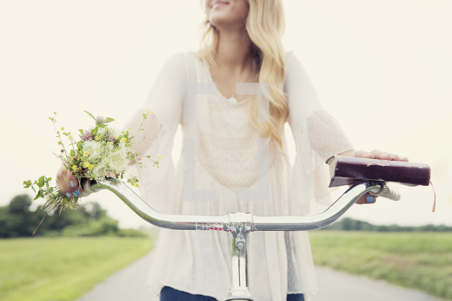 teenage girl riding a bicycle holding a book and flowers.