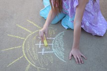 A little girl drawing three Easter crosses with sidewalk chalk 